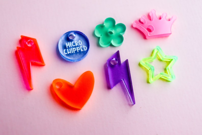 Pu&ograve; includere: Assortimento di ciondoli in acrilico colorati in varie forme, tra cui un cuore, un fulmine, una stella, un fiore, una corona e un ciondolo rotondo con il testo "MICRO CHIPPED".