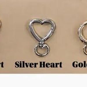 May include: Three metal clasps on a tan background. The clasps include a gold heart, a silver heart, and a gold clasp. The text below each clasp reads "Gold Heart", "Silver Heart", and "Gold Clasp".