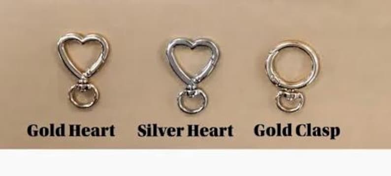 May include: Three metal clasps on a tan background. The clasps include a gold heart, a silver heart, and a gold clasp. The text below each clasp reads "Gold Heart", "Silver Heart", and "Gold Clasp".
