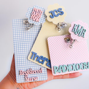 Puede incluir: Tres portatarjetas rectangulares con patrones de cuadros vichy en azul, amarillo y rosa. El azul incluye el texto "Faith Over Fear" y "Registered Nurse". El amarillo muestra "JCS" y "Therapy". El rosa presenta "KMR" y "RADIOLOGY".