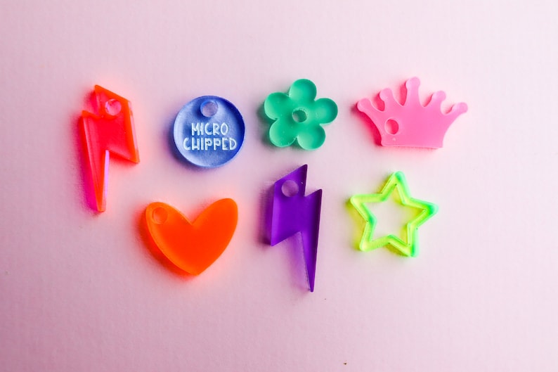 Pu&ograve; includere: Assortimento di ciondoli in acrilico colorati in varie forme, tra cui un cuore, una stella, un fulmine, un fiore, una corona e un cerchio con il testo "MICRO CHIPPED".