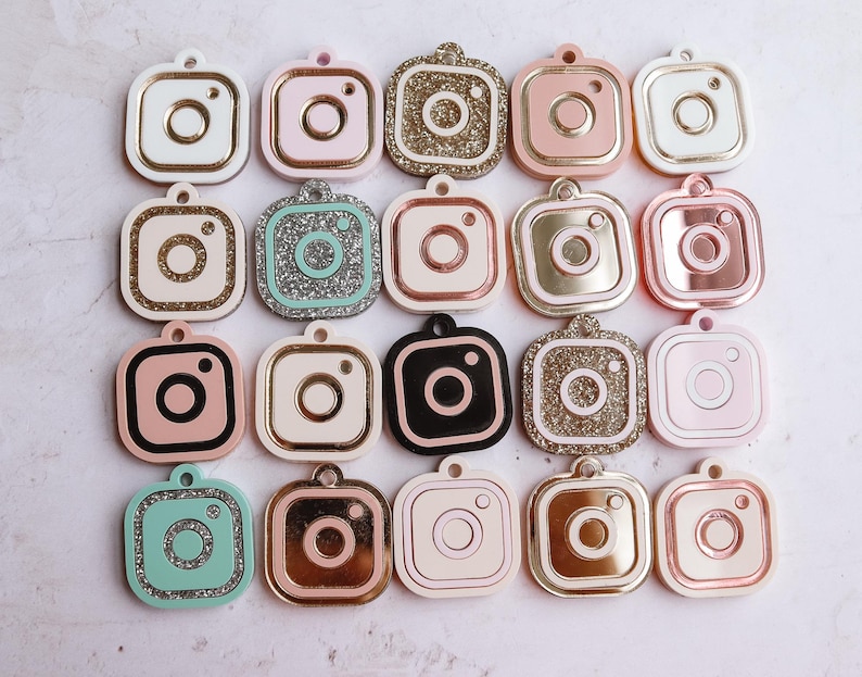 May include: Twenty assorted camera-shaped charms with various colors and finishes, including glitter, solid colors, and metallic finishes.