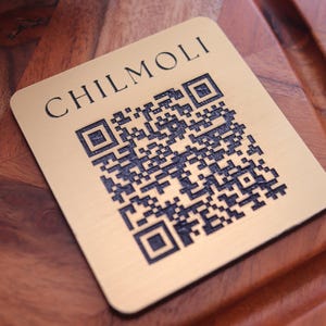 Peut inclure: Une &eacute;tiquette en m&eacute;tal couleur or avec le texte "CHILMOLI" et un code QR noir et blanc.