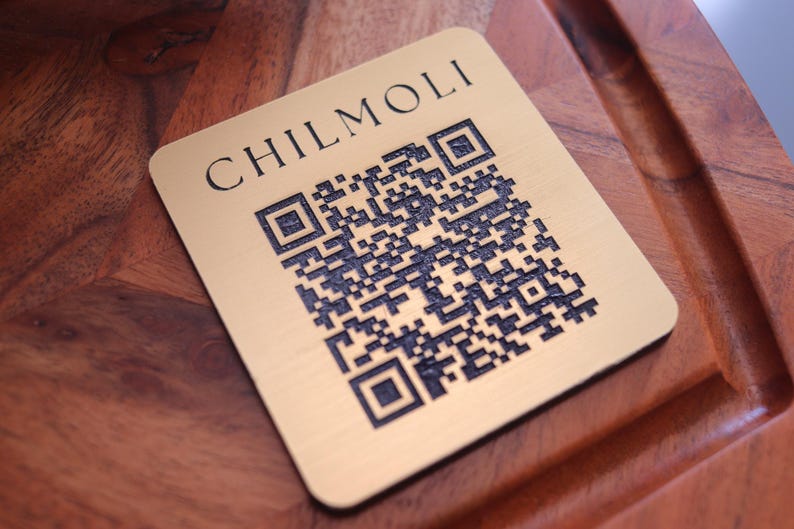 Peut inclure: Une &eacute;tiquette en m&eacute;tal couleur or avec le texte "CHILMOLI" et un code QR noir et blanc.