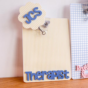 Puede incluir: Un porta credenciales de rayas verticales amarillas y blancas con un remate festoneado que presenta las letras azules JCS y el texto azul Therapist en la parte inferior. Al lado hay un porta credenciales de cuadros azules y blancos con texto rosa Registered Nurse.