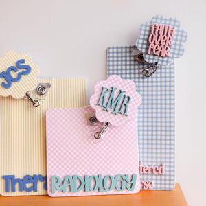 Puede incluir: Tres portatarjetas rectangulares con adornos circulares festoneados. Uno amarillo a rayas con JCS azul, uno rosa a cuadros con KMR y RADIOLOGY en azul verdoso, y uno azul a cuadros con el texto rosa FAITH OVER FEAR. Cada uno incluye cord&oacute;n retr&aacute;ctil.
