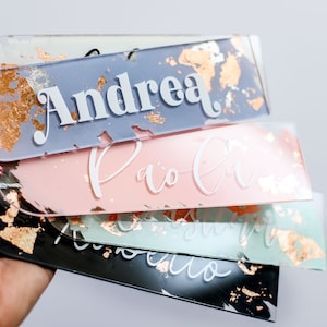 May include: A stack of four personalized acrylic bookmarks with gold foil accents. The names "Andrea", "Paola", "Isabella", and "Roberto" are written in white on the bookmarks.