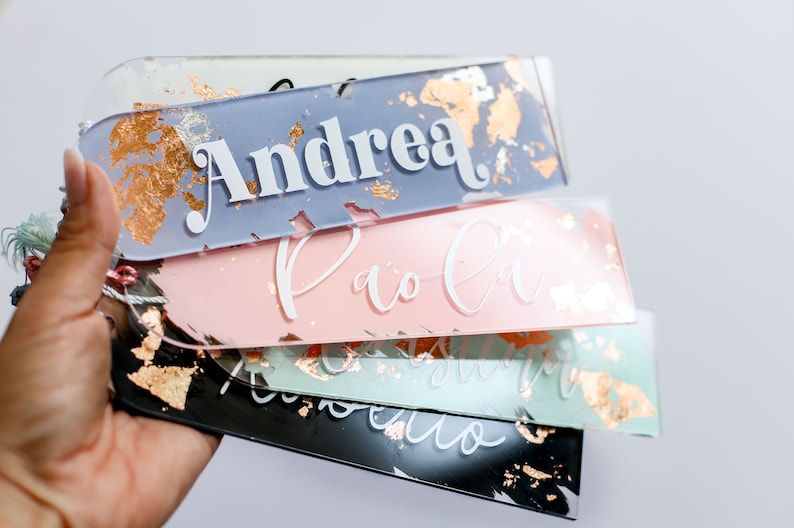 May include: A stack of four personalized acrylic bookmarks with gold foil accents. The names "Andrea", "Paola", "Isabella", and "Roberto" are written in white on the bookmarks.