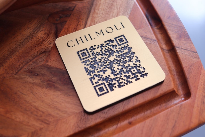 Peut inclure: Une plaque carr&eacute;e dor&eacute;e avec le texte "CHILMOLI" et un code QR noir et blanc.