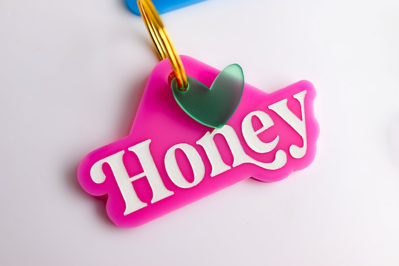 Pu&ograve; includere: Portachiavi in plastica rosa con la parola "Honey" in lettere bianche e un ciondolo a forma di cuore verde.