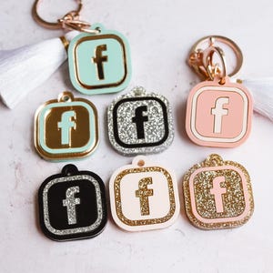 May include: Set of ten keychains featuring the Facebook logo in various colors and finishes. The keychains are made of metal and plastic and have a variety of designs, including glitter, solid colors, and silver.
