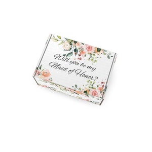 May include: A white gift box featuring the text "Will you be my Maid of Honor?" surrounded by floral illustrations. The box is adorned with watercolour roses and foliage, ideal for a wedding proposal or bridesmaid gift.
