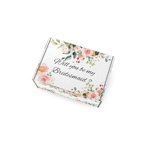 May include: White gift box with floral accents in peach, pink, and green. The box is decorated with roses and greenery. Text on the box reads, "Will you be my Bridesmaid?" Ideal for wedding proposals.