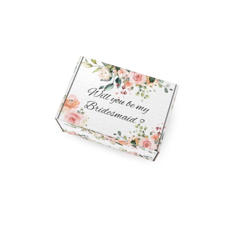 May include: White gift box with floral accents in peach, pink, and green. The box is decorated with roses and greenery. Text on the box reads, "Will you be my Bridesmaid?" Ideal for wedding proposals.