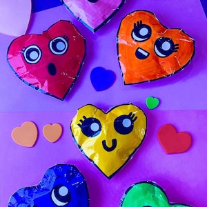 May include: Six heart-shaped crafts with different colored backgrounds and cartoon faces. The hearts are pink, red, orange, yellow, blue, and green.