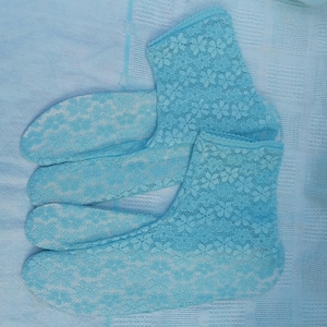 Può includere: Un paio di calzini in pizzo azzurro con un motivo floreale. I calzini sono realizzati in un materiale delicato e trasparente e sono appoggiati su uno sfondo di tessuto azzurro chiaro. I calzini sono di un colore pastello tenue.