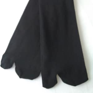 Op de afbeelding: Een paar zwarte tabi-sokken, ontworpen met een gespleten teen voor traditioneel Japans schoeisel. De sokken zijn gemaakt van een effen, ondoorzichtig zwart materiaal en liggen op een witte ondergrond.