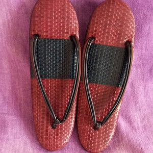 Könnte beinhalten: Ein Paar dunkelrote und schwarze gewebte Ledersandalen mit schwarzen Riemen.