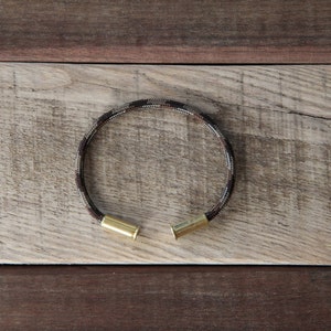 May include: A camouflage patterned bracelet with two gold bullet casings as clasps.