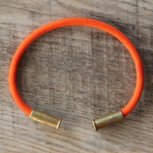 May include: Orange paracord bracelet with brass bullet casings as clasps.