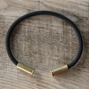 May include: A black paracord bracelet with two brass bullet casings as clasps.