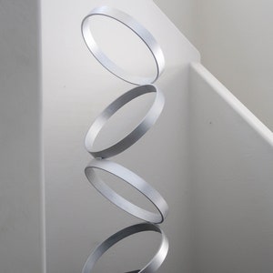May include: A silver metal sculpture of four stacked rings on a black square table with a white background.