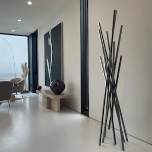 May include: A modern interior design with a black and white abstract painting, a gray chair, a wooden table, and a tall, silver metal sculpture.