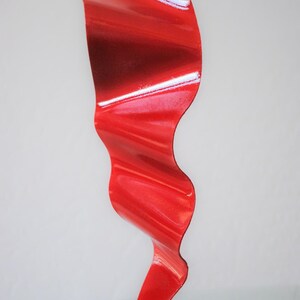 May include: A red metal sculpture with a wavy, abstract design. The sculpture is standing on a white base.