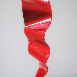 Op de afbeelding: Een rood metalen beeldhouwwerk met een golvend, abstract ontwerp. Het beeldhouwwerk staat op een witte basis.