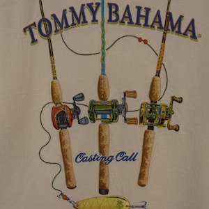 May include: Cream-colored fabric with a design featuring three fishing rods with reels and a lure. The rods are brown with colorful reels in orange, green, and yellow. The text "TOMMY BAHAMA" is arched across the top, and "Casting Call" is below the rods.