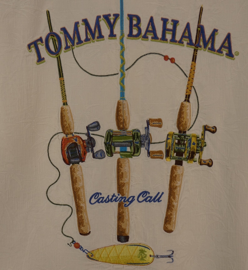 May include: Cream-colored fabric with a design featuring three fishing rods with reels and a lure. The rods are brown with colorful reels in orange, green, and yellow. The text "TOMMY BAHAMA" is arched across the top, and "Casting Call" is below the rods.