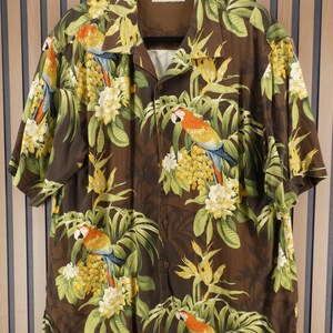 May include: Brown button-down shirt with a tropical parrot and floral print. The short-sleeved shirt features a vibrant design with parrots, yellow flowers, and green leaves. The shirt has a classic collar and is made of a lightweight fabric.
