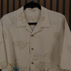 K&ouml;nnte beinhalten: Cremefarbenes Button-Down-Hemd mit Bl&auml;ttermuster. Das Hemd hat kurze &Auml;rmel und einen klassischen Kragen. Der Markenname "Tommy Bahama" ist auf dem Kragen gestickt. Das Hemd ist aus leichtem Stoff, ideal f&uuml;r warmes Wetter.