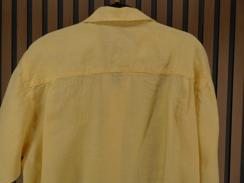 May include: A pale yellow button-down shirt made from a lightweight material. The shirt features a classic collar and a relaxed fit, suitable for casual wear. The back of the shirt is visible, showing the yoke and the fabric's texture.