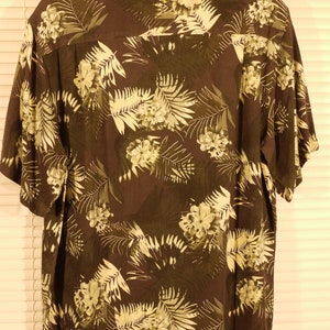 May include: A dark brown short-sleeved shirt with a tropical print featuring white flowers and green leaves.