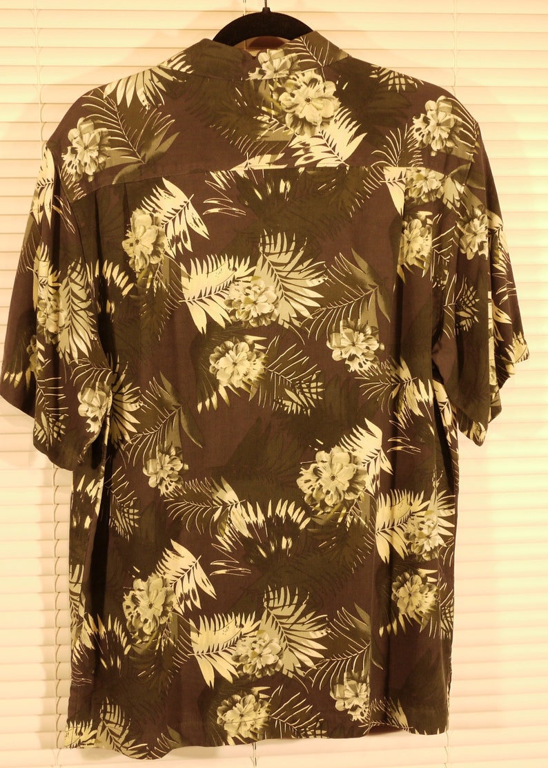 May include: A dark brown short-sleeved shirt with a tropical print featuring white flowers and green leaves.