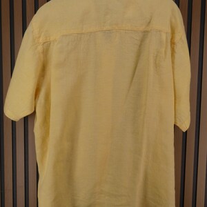 May include: A short-sleeved, yellow button-down shirt. The shirt is made of a lightweight fabric and features a classic collar and a relaxed fit. The back of the shirt is visible, showing the yoke and the texture of the material.