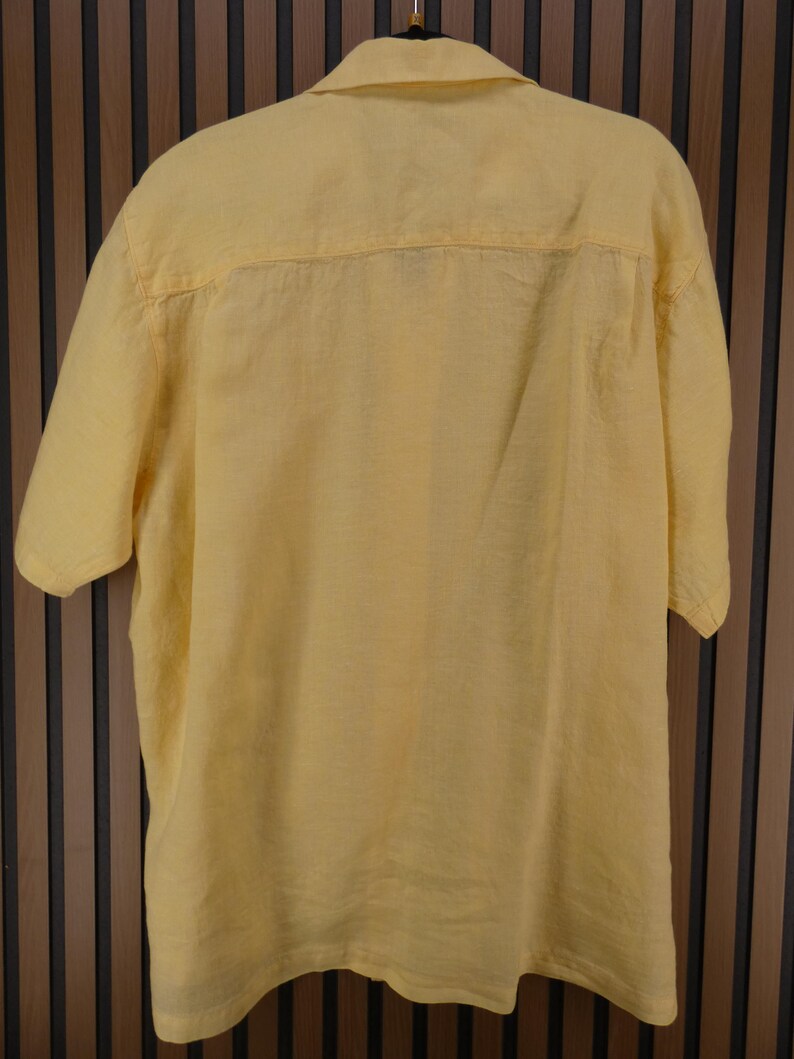 May include: A short-sleeved, yellow button-down shirt. The shirt is made of a lightweight fabric and features a classic collar and a relaxed fit. The back of the shirt is visible, showing the yoke and the texture of the material.