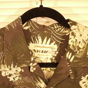 May include: A dark green and white tropical print button-up shirt with a Tommy Bahama label and the words "Original Fit".