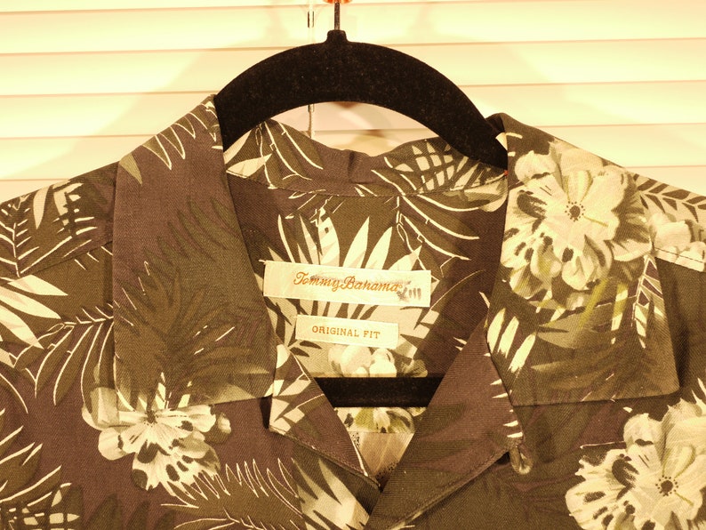 May include: A dark green and white tropical print button-up shirt with a Tommy Bahama label and the words "Original Fit".