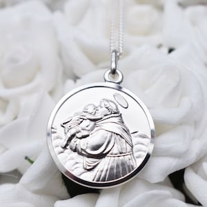 May include: Silver pendant necklace featuring a detailed image of Saint Anthony of Padua holding a baby Jesus. The pendant is round and has a halo above Saint Anthony's head.