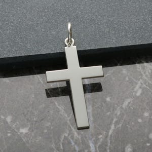 May include: A silver cross pendant with a simple design. The cross is smooth and has a shiny finish.