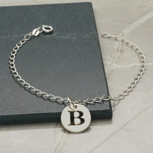 以下が含まれることがあります： 太字の「B」が刻まれた丸いチャームが付いたシルバーチェーンブレスレットです。