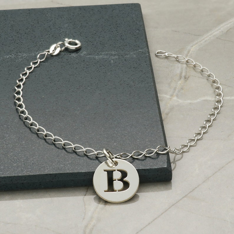 以下が含まれることがあります： 太字の「B」が刻まれた丸いチャームが付いたシルバーチェーンブレスレットです。