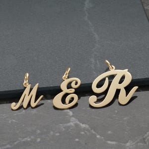 May include: Three gold-coloured metal charms in the shape of the letters M, E, and R. The letters are in a cursive font and are slightly raised.