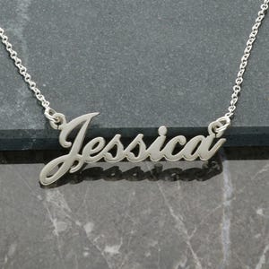 May include: Silver necklace with the name "Jessica" spelled out in a cursive font.