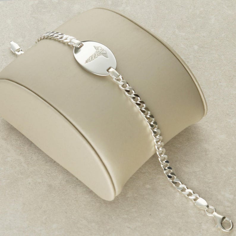 Puede incluir: Un brazalete de cadena de plata con un dije ovalado de plata con un s&iacute;mbolo m&eacute;dico.
