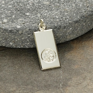 May include: Silver pendant with a rectangular shape and a raised image of a saint inside a circle.