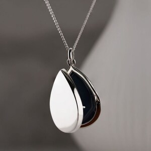 May include: A silver teardrop-shaped locket necklace with a hinged opening. The locket is open, revealing a black interior.