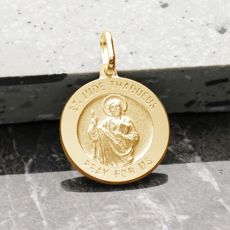May include: Gold-toned St. Jude Thaddeus medal pendant with a raised image of the saint and the inscription "St. Jude Thaddeus Pray For Us".